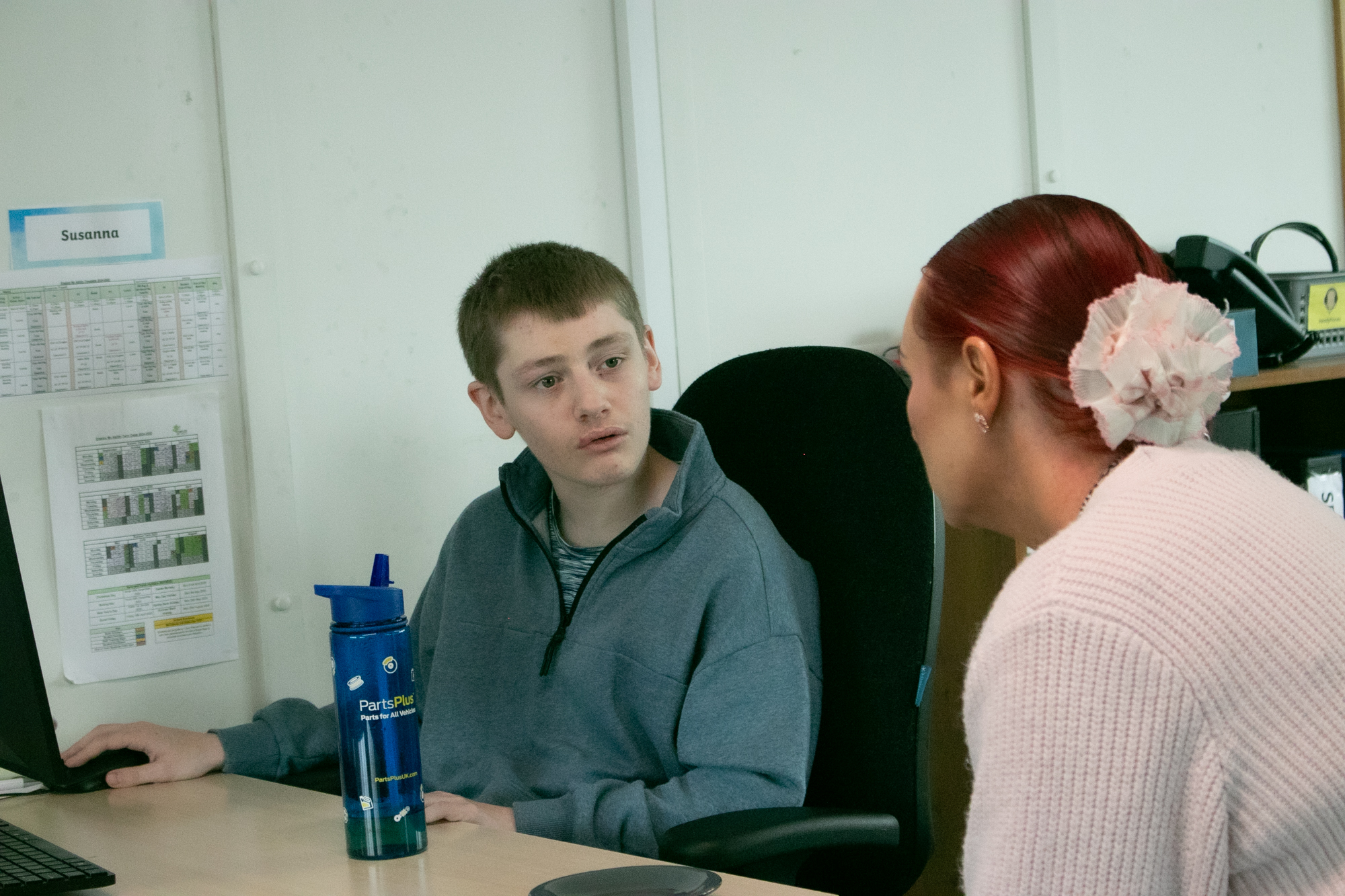 a student is shown speaking to a learning support worker while sat at a computer